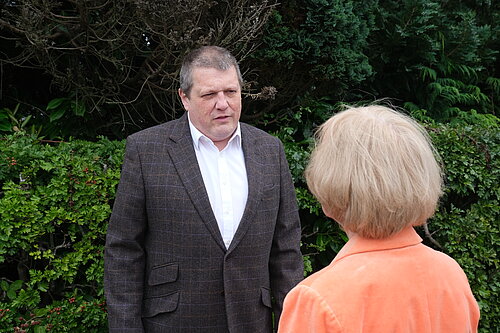 Ben Langmead in a grey blazer and white shirt listing and chatting with a resident.