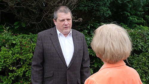 Ben Langmead in a grey blazer and white shirt listing and chatting with a resident.