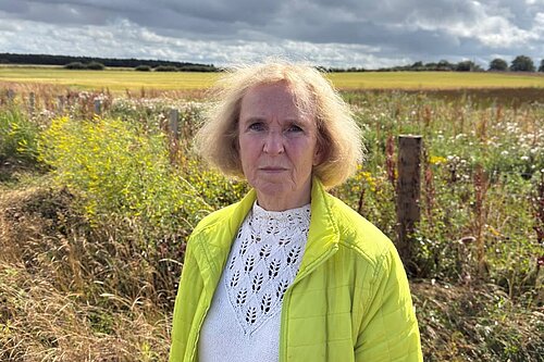 Susan Murray in front of green farmlands.