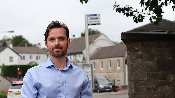 Adam Harley in a blue shirt with a bus stop in the background.