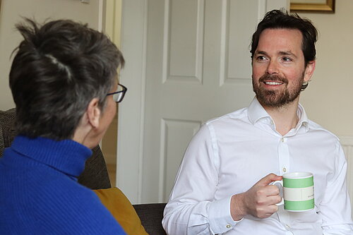 Adam Harley sitting down with a mug talking with a resident.