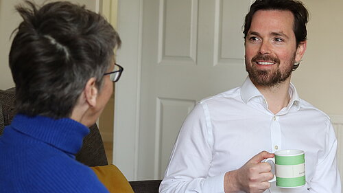 Adam Harley sitting down with a mug talking with a resident.