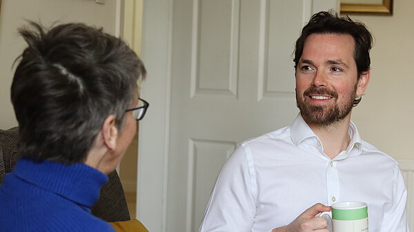 Adam Harley sitting down with a mug talking with a resident.