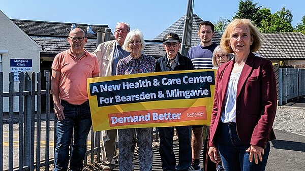 Susan Murray standing in front of a group of campaigners holding up a banner saying a new health and care centre for Bearsden and Milngavie