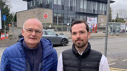 Vaughan Moody and Adam Harley standing on the pavement with Bearsden Community Hub in the background surrounded by metal fencing.