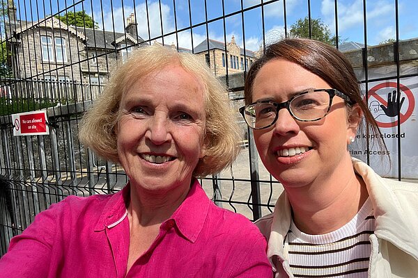 Susan Murray and Aileen Polson in front of a fence outside Milngavie Primary School.