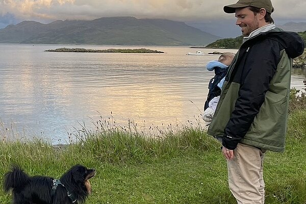 Adam Harley with his child and dog at the edge of water.