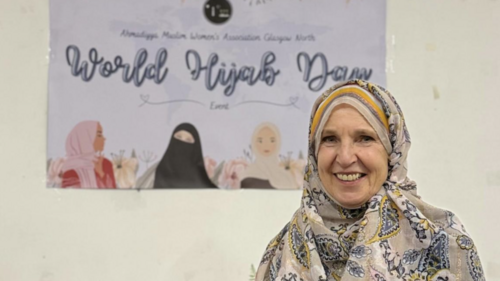 Susan Murray wearing a light coloured Hijab with a poster in the background for World Hijab Day